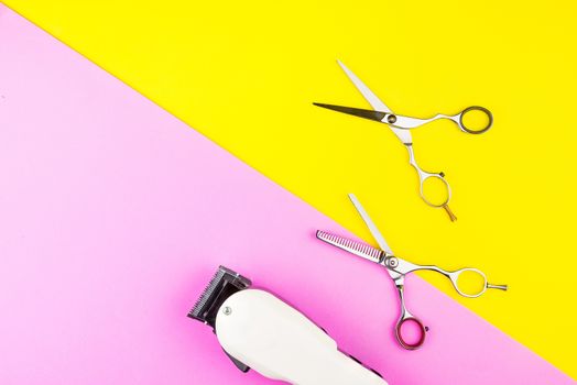 Stylish Professional Barber Scissors and White electric clippers on yellow and pink background. Hairdresser salon concept, Hairdressing Set. Haircut accessories. Copy space image, flat lay