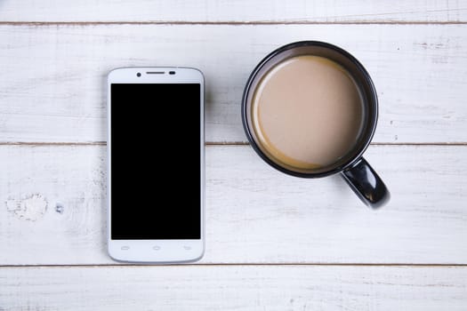 smartphone and coffee cup on the white wooden background.