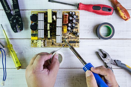 Serviceman soldering circuit board with soldering iron in the service workshop.