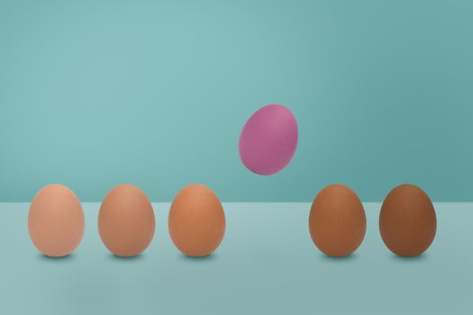 Flying pink egg and  different shades color of eggs on blue background. Minimal Easter idea concept.