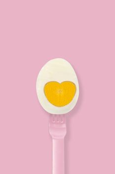 Half boiled egg on a pink fork on pink background, minimal eater concept.