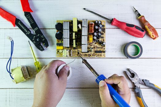 Serviceman soldering circuit board with soldering iron in the service workshop.