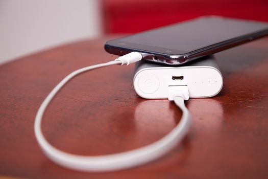 Mobile Phone Charging With Power Bank on wooden table, USB cord pluged
