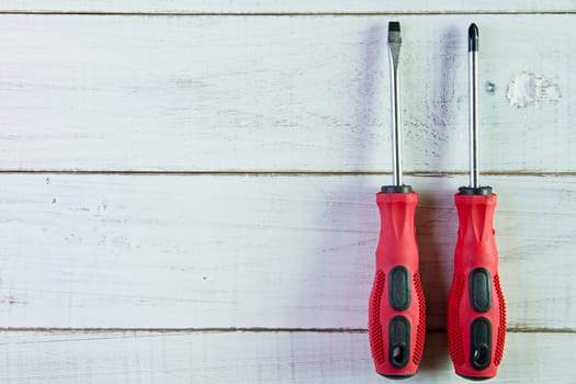 Two screwdrivers with the red handle on the white wooden background