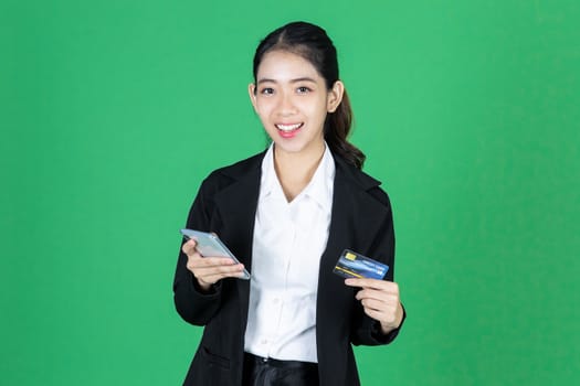 Portrait of cheerful young Asian business woman holding mobile smart phone and credit card on green isolated background. Internet of things concept.