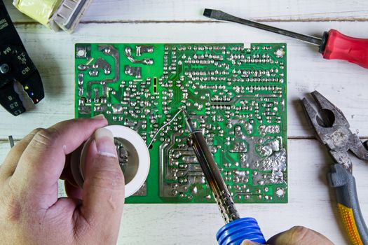 Serviceman soldering circuit board with soldering iron in the service workshop.