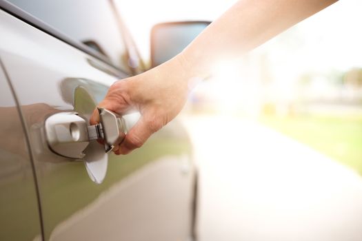 Woman's hand pulling a car's door handle in the park.