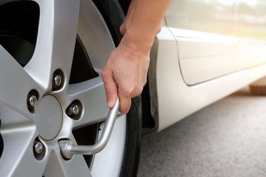 Hand changing tire with car wrench.