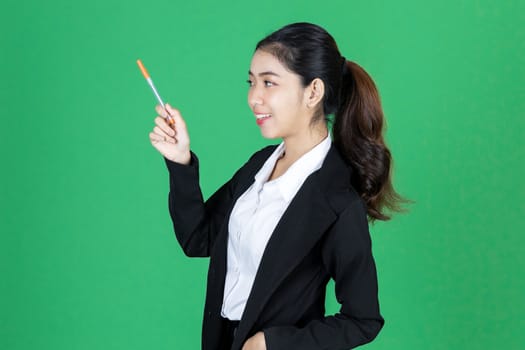 Portrait of attractive young Asian business woman holding pen and having idea posing on green isolated background.