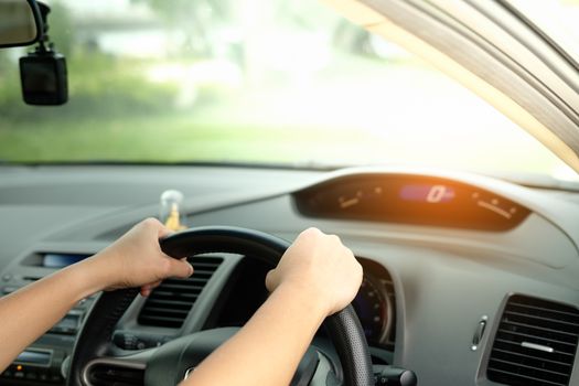 The hands are holding the steering wheel and driving on a light day.