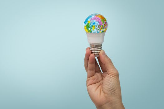 Hand is holding the LED bulb with the globe on blue background.