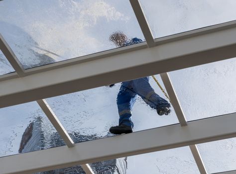 Male worker washing large expanse of glass roof over swimming pool with hose pipe