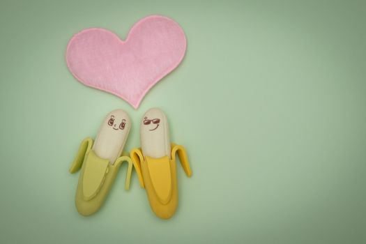 Two rubber banana and heart-shape pillow on green background, valentine concept.