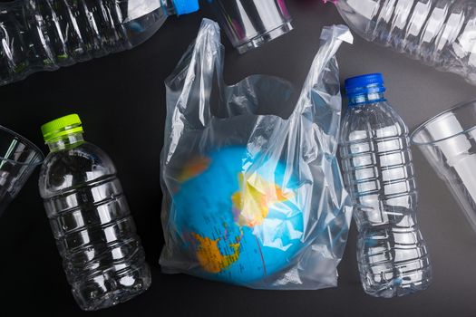 Earth world globe and plastic bottle waste on the black background.Saving the planet Earth from plastic bags concept.Global warming.Plastic waste overflows the world
