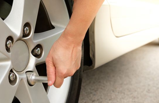 Hand changing tire with car wrench.