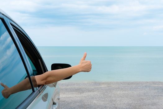 Happy woman raised arms from the car parked in the sea on a bright day.