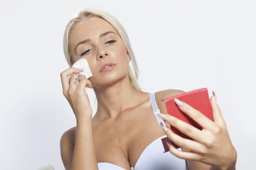 Young woman clean face and eyes with wet wipes, holding mirror, remove make-up, body breast lingerie