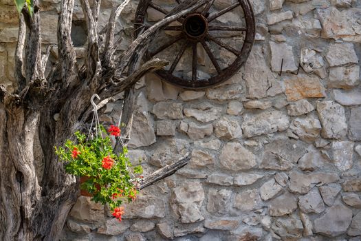 Dead tree branches and cartwheel on stone farmhouse wall with red geranium flowers