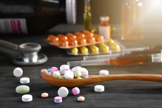 Assorted pharmaceutical medicine pills, tablets and capsules in wooden spoon on a black wooden background. Medicine concepts. Minimalistic abstract concept. Selected focus