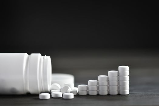 White medical pills and tablets spilling out of a drug bottle. top view with copy space. On Black wood Background. Natural herbs, organic pills, vitamins from medicinal plants. Alternative medicine. 