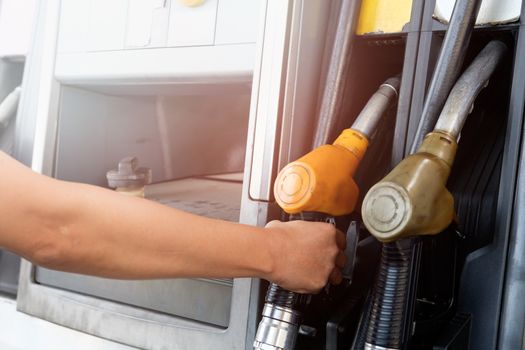 The gold car is filling the fuel at the oil station. Hand holding Fuel nozzle in gas pump.