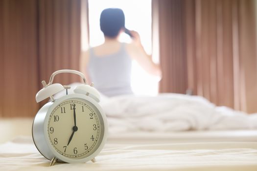 The alarm clocks in the morning, causing the woman to wake up and talking on the phone.