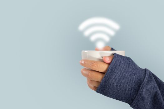 Girl's hand in sweater holding a cup of coffee with wi-fi symbol isolated on blue background.