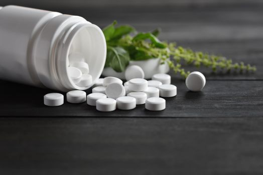 White medical pills and tablets spilling out of a drug bottle. top view with copy space. On Black wood Background. Natural herbs, organic pills, vitamins from medicinal plants. Alternative medicine. 