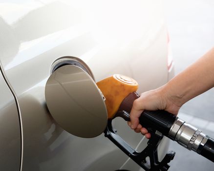 The gold car is filling the fuel at the oil station. Hand holding Fuel nozzle in gas pump.