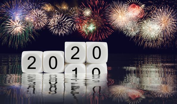 Composite of multiple firework explosions with calendar blocks showing 2019 sinking into the ocean as 2020 starts