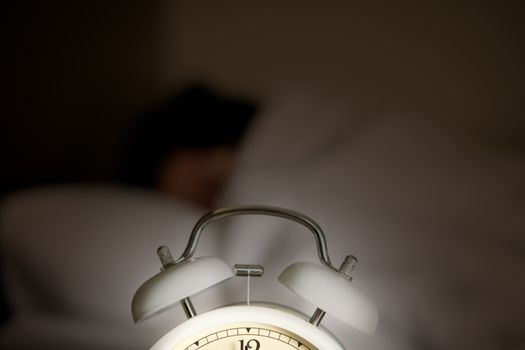 A glowing alarm clock is placed in front of a sleeping woman.