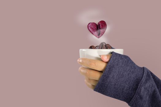 The hands of a woman in a sweater holding a glass of coffee beans and pink heart coffee bean floats over the glass, Valentine and love concept.