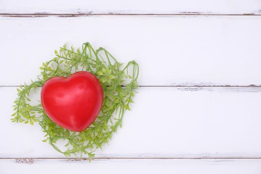 Red heart is in the bird's nest from leaves on the white wooden background, valentine concept with copy space.
