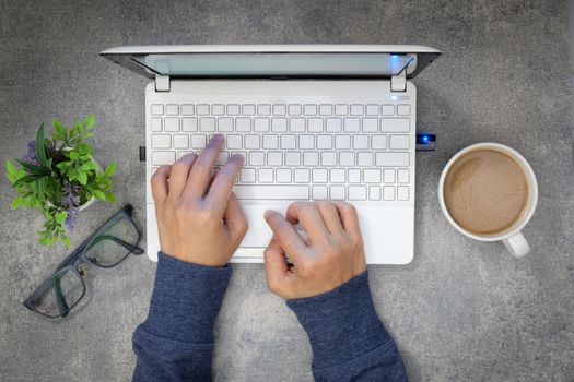 The woman's hand in sweater is printing a white computer with a cup of coffee on dark table.