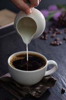 Classic still life with The hand is pouring milk to a cup of coffee with copy space, verticle picture.