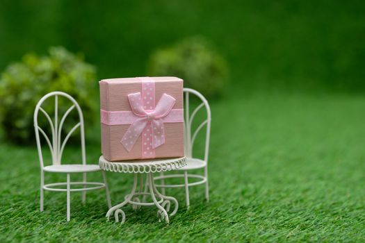 Gift box on white field chair in green garden, with copy space to write.