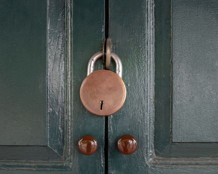 Antique locked with old rusted padlock on green door background.