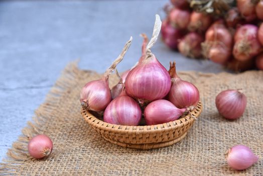Thai red onion or Shallots. Fresh purple shallots on bamboo basket with old wallpaper and shallots bunch background. Selected focus. Concept of spices in healthy cooking