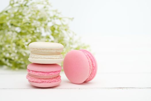 Macaroons and flowers on the white wooden background.