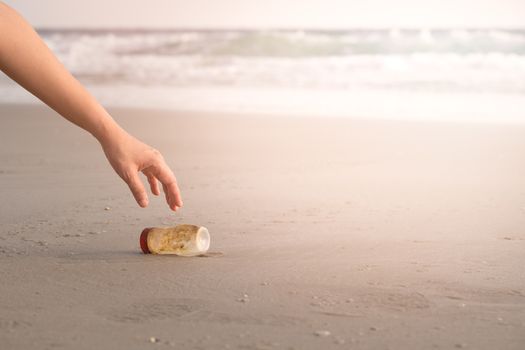 The hand of a woman is picking up a plastic bottle to clean the beach.