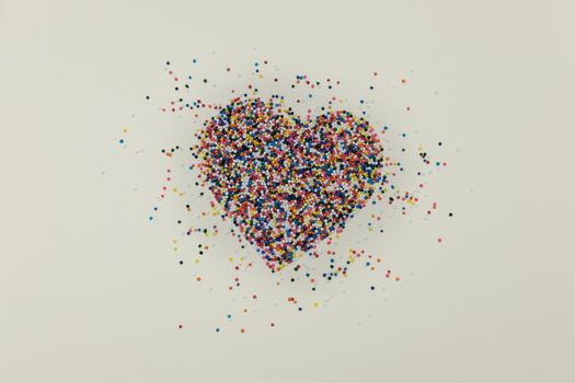 Heart-shape colorful sprinkles spilled on yellow background, valentine concept.