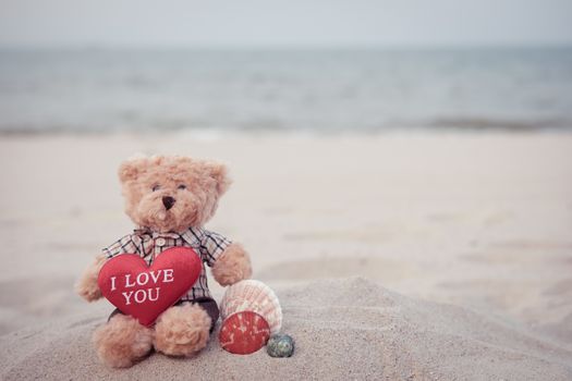 Teddy Bear with red heart sitting by the sea.