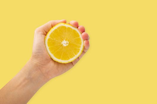 Female hand squeezing half of lemon on yellow background, Healthy eating and diet concept.