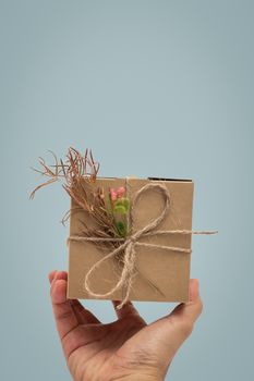 Hand holding a present, gift box rustic style on blue background.
