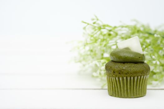 Green tea cupcake and flowers on the white wooden background.