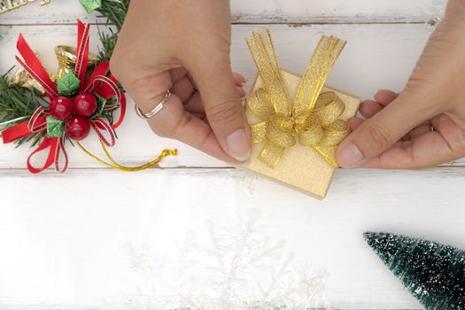Top view of female hands tying a golden bow on a gift box.