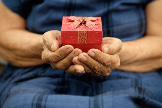 Wrinkled old hands holding little gift with red bow.