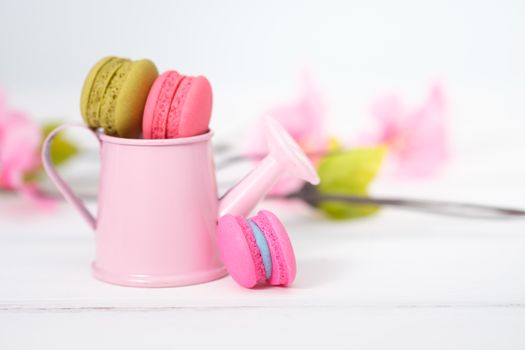 Macaroons and flowers on the white wooden background.