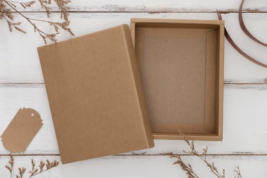Opened cardboard box on white wooden background with dry grass.
