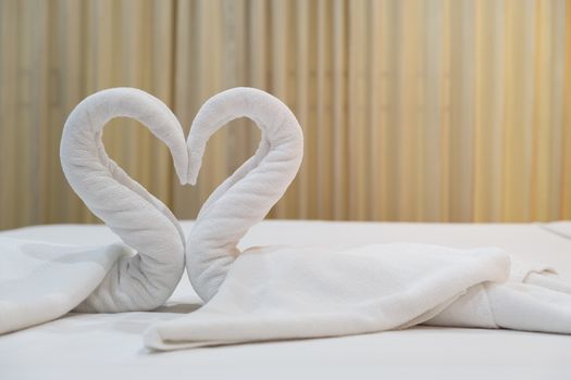 Close-up folded swans bird of fresh white bath towels on the bed sheet in the hotel.